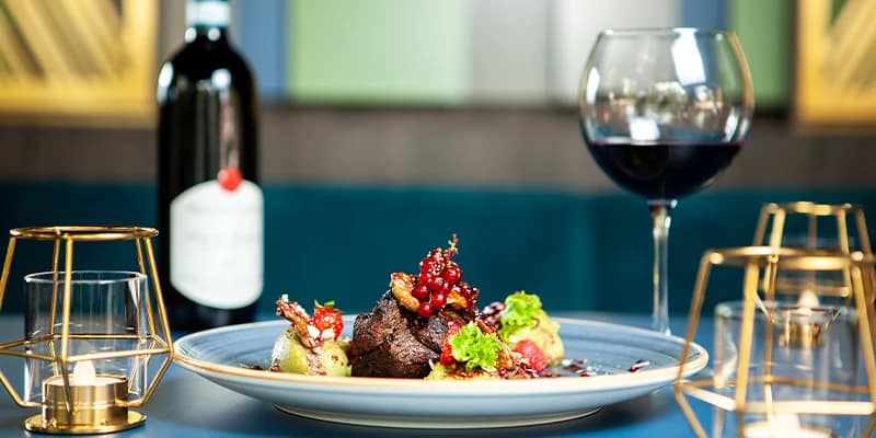 Ein Teller mit fein gekochtem Fleisch und Beilagen mit einem Glas Wein und Kerzen auf dem Tisch