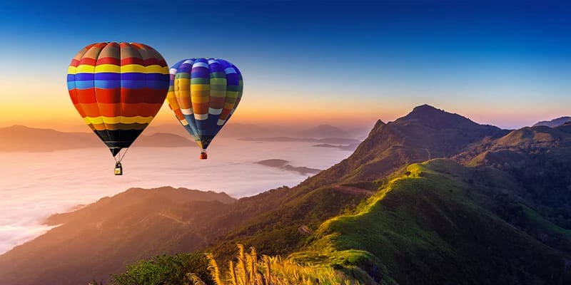 Zwei Heißluftballons schweben hoch am Himmel über den Bergen bei Sonnenuntergang