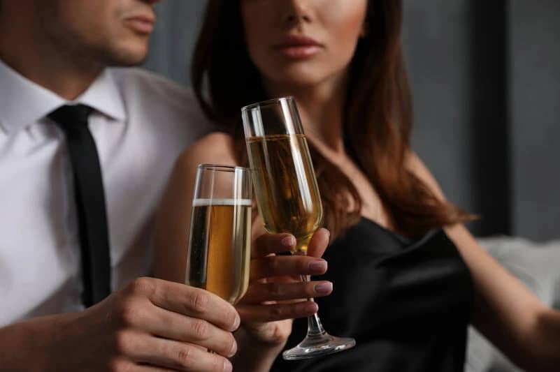 Ein Mann und eine Frau halten Gläser Champagner, Escort Begleitservice erkunden.