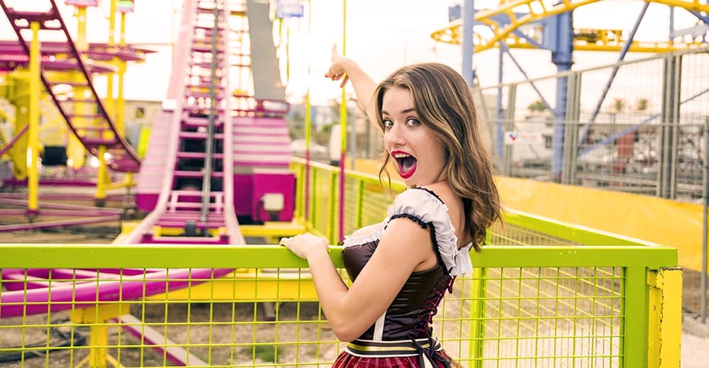 Eine aufgeregte junge Frau auf dem Cannstatter Volksfest, die auf eine Achterbahnfahrt zeigt